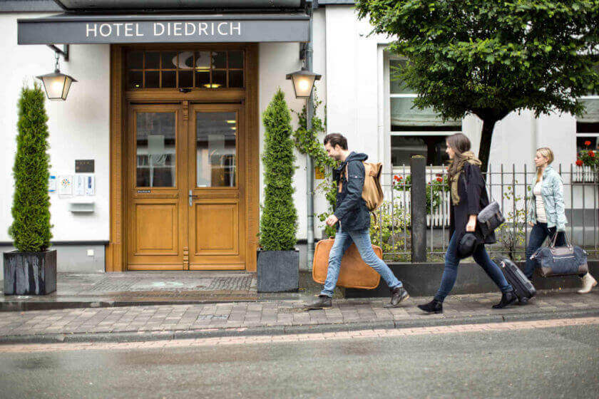 Drei Personen reisen an und gehen mit ihren Koffern auf den Hoteleingang zu