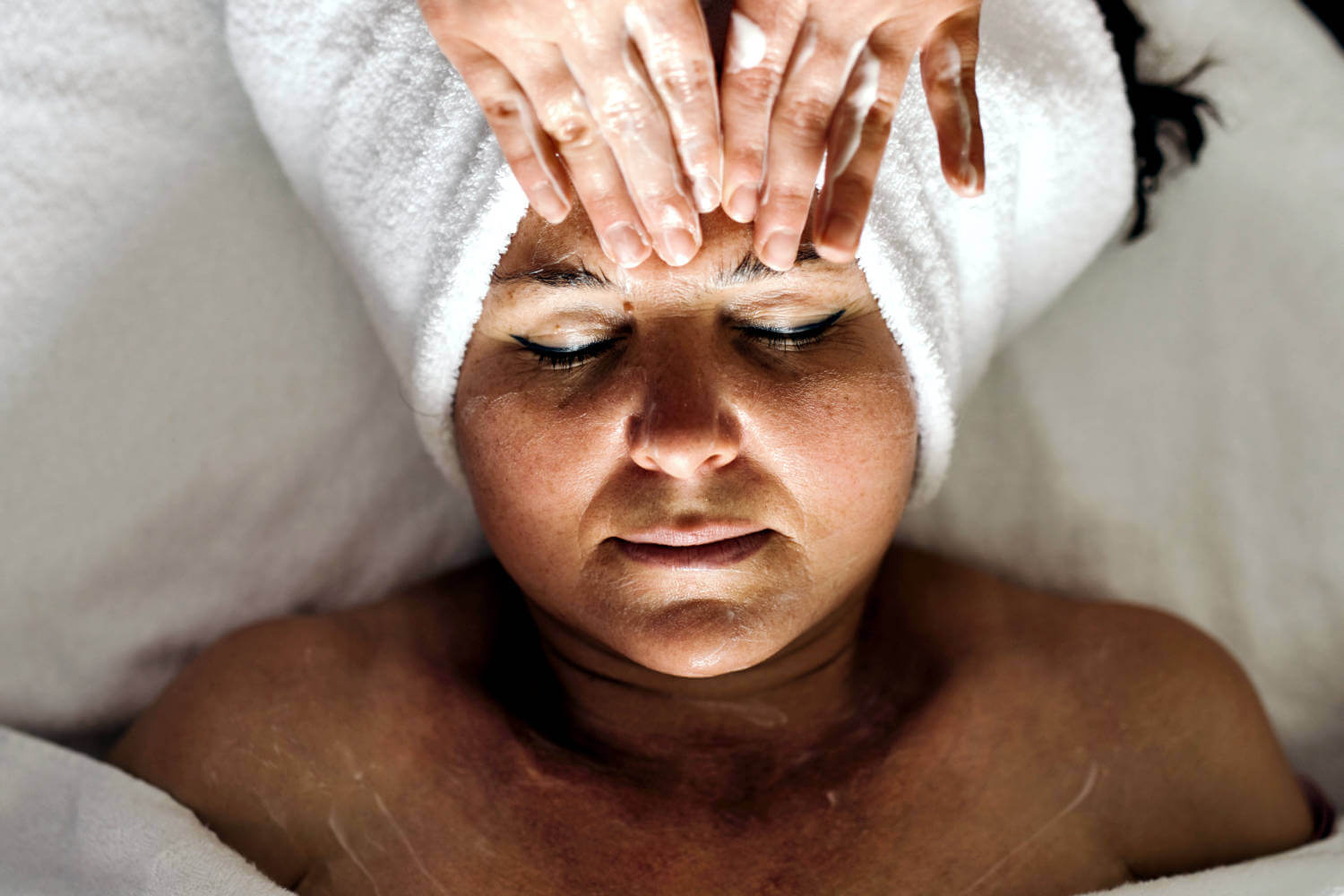 Eine liegende und in Frottee gewickelte Frau bekommt eine Stirnmassage