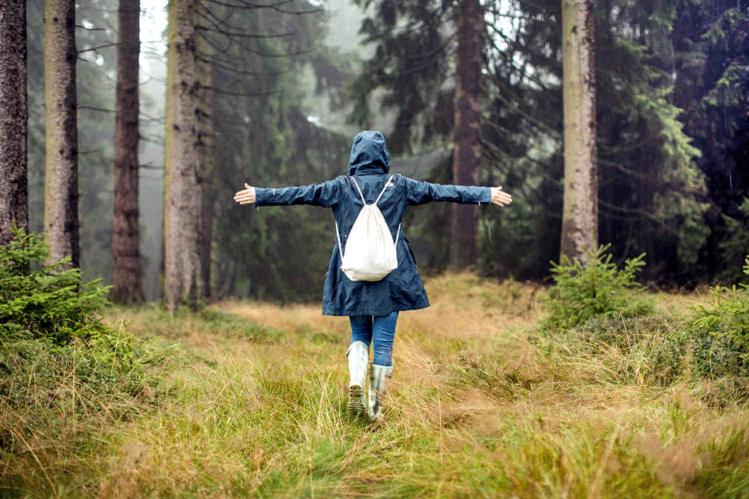 Eine Frau steht im saftig grünen Wald und streckt beide Arme frei von sich