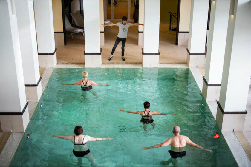 Der Kursleiter steht am Rand des Innenpools und macht den Teilnehmern die Aquagymnastik-Übungen vor im Hotel Diedrich