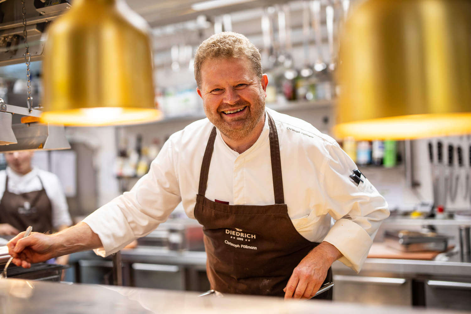 Küchenchef Christoph Pöllmann lächelt während der Arbeit in der Küche in die Kamera - Hotel Diedrich