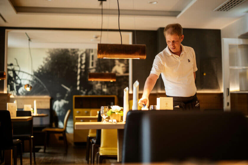A service employee lights the candle on a table in the Alte Post restaurant - Hotel Diedrich