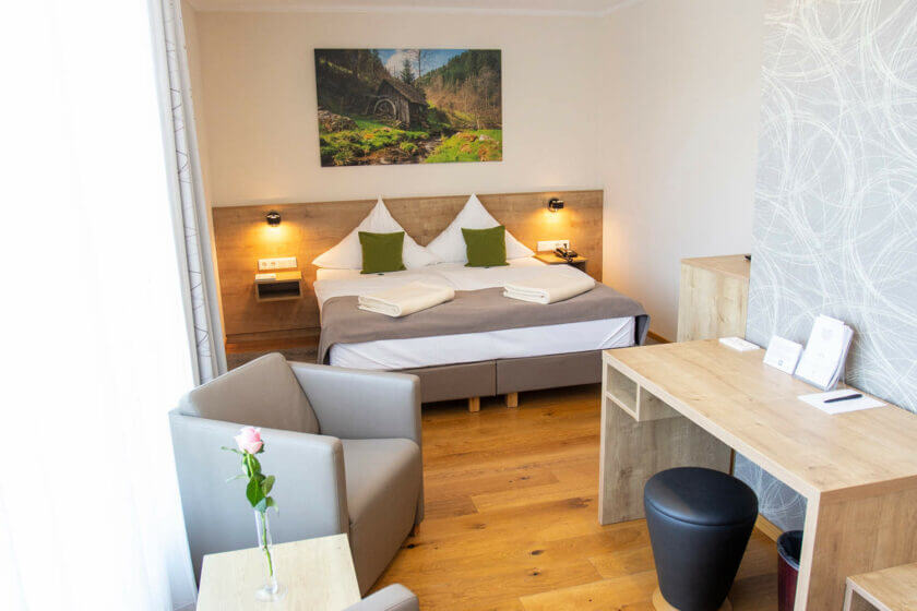 Blick auf das Bett, den Schreibtisch und den Sessel im gemütlichen Doppelzimmer "Stammhaus A Talseite" im Hotel Diedrich, Hallenberg