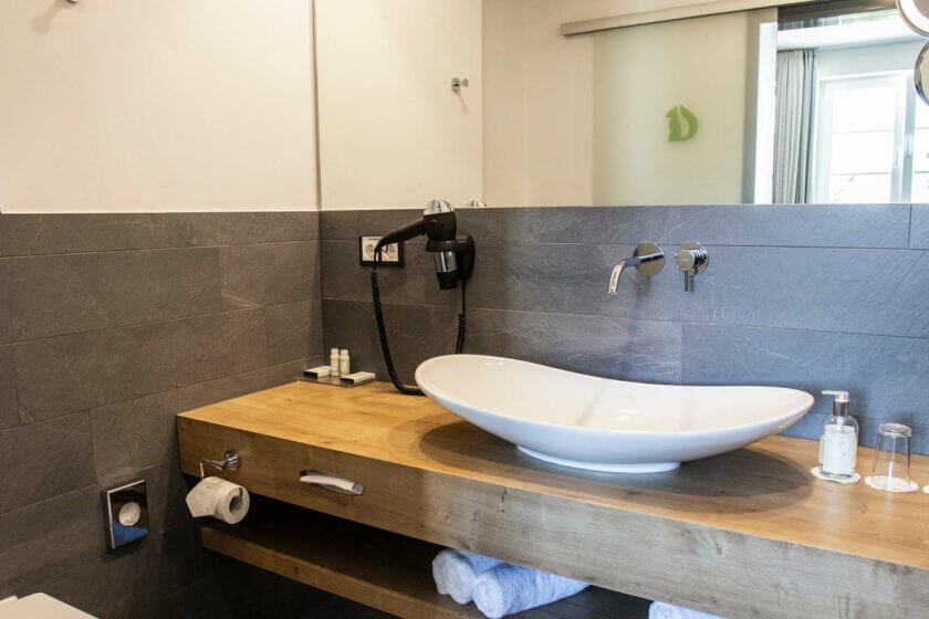 Ovaler Waschtisch auf Holzunterbau im Badezimmer des Doppelzimmers "Stammhaus Premium Plus Talseite" im DIEDRICH Wellnesshotel & SPA, Hallenberg