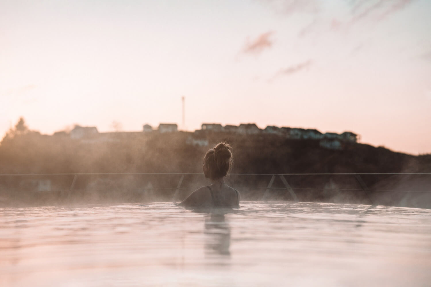 Eine Frau steht während der Morgensonne im dampfenden Außenpool und schaut in die Ferne