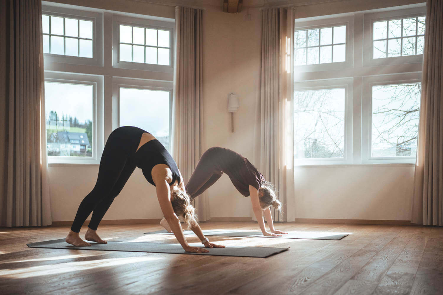 Zwei Frauen machen im Yogahaus eine Übung, bei der sie mit den Fußspitzen und den Fingerspitzen den Boden berühren.