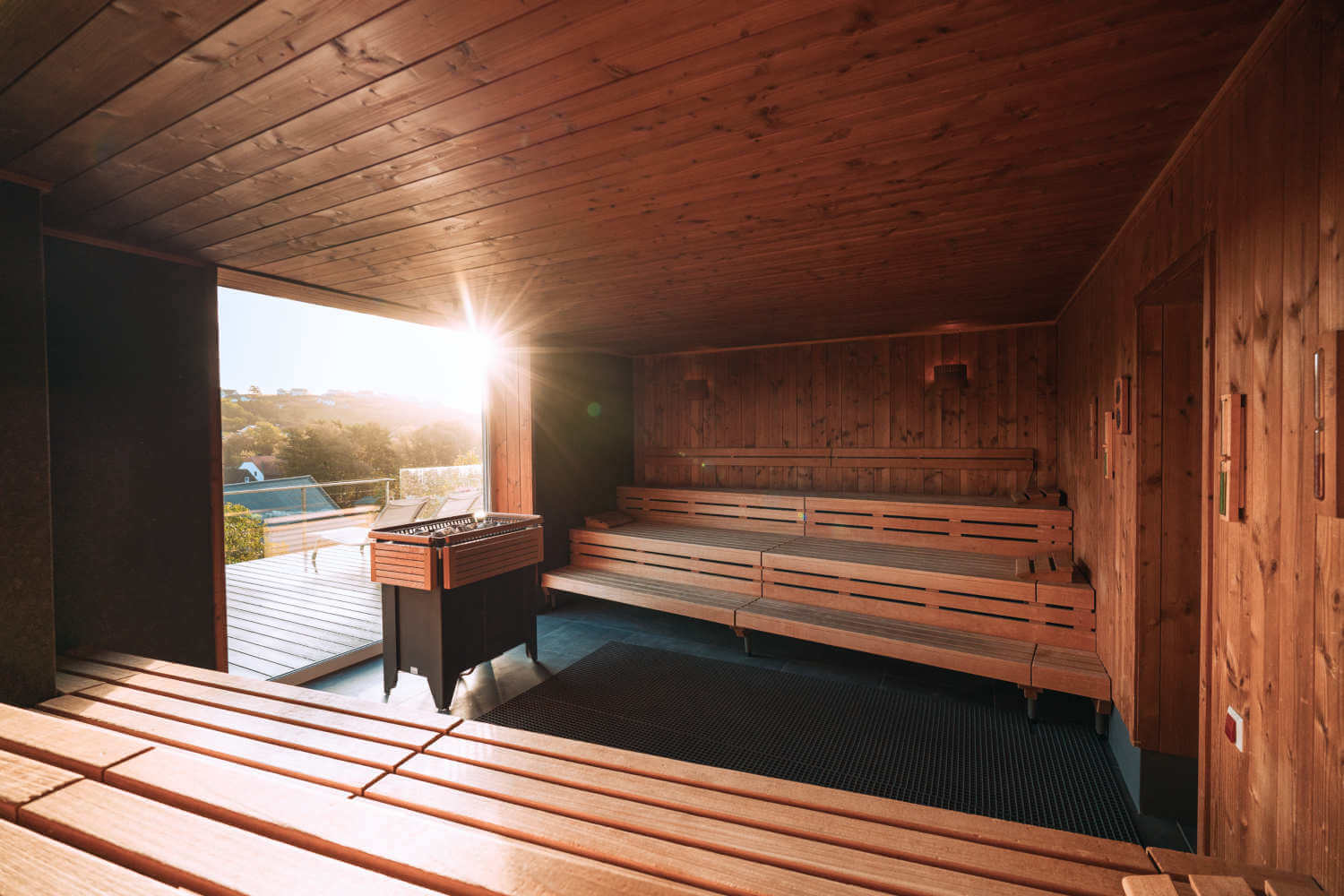 Aufnahme der Finnische Sauna mit Blick nach draußen durch das große Panoramafenster, durch das die Sonnenstrahlen hineinscheinen