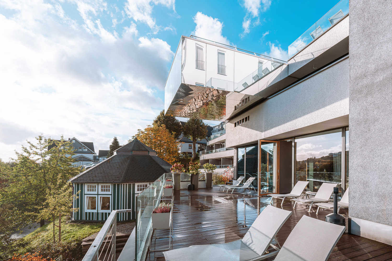 Moderne Terrasse mit Glasgeländern und eleganten Liegestühlen, Blick auf traditionelle Häuser.