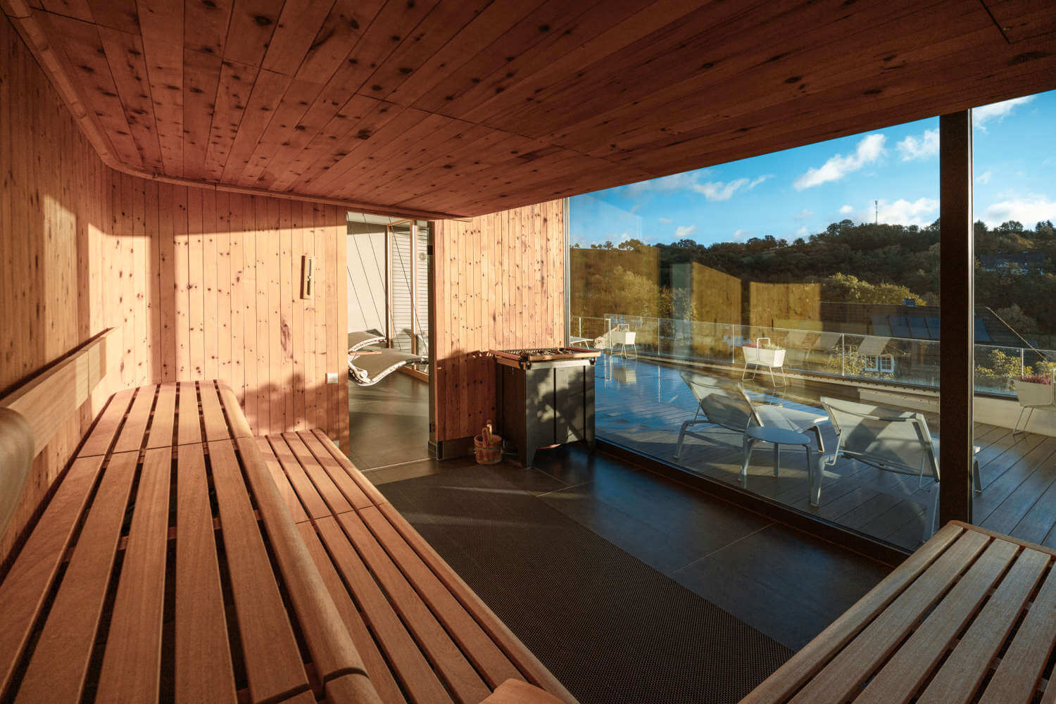 Innenansicht einer Sauna im Wellnesshotel Diedrich im Sauerland mit Blick auf eine Terrasse und das umliegende Hügelland durch eine Panoramaverglasung, sonnendurchflutet für ein entspannendes SPA-Erlebnis in NRW.