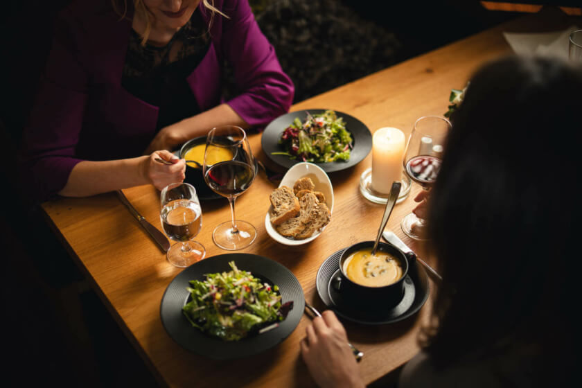 Zwei Frauen genießen ein Abendessen bei Kerzenlicht im Restaurant, mit Wein und gesundem Essen.