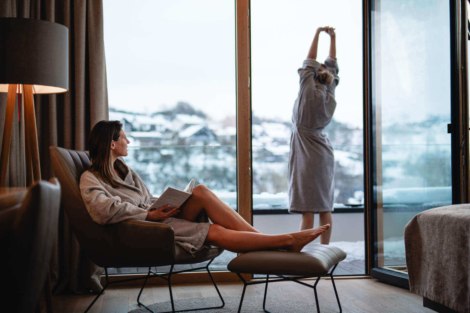 Eine Frau im Bademantel steht im Winter auf ihrem Zimmerbalkon und streckt sich genüsslich im Wellnesshotel Sauerland