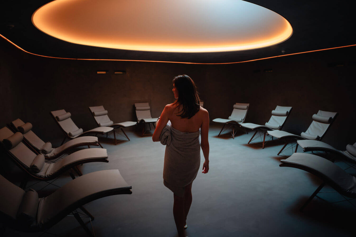 Eine Frau betritt elegant den Nachruheraum des Saunabereichs im Hotel Diedrich mit im Kreis angeordneten Liegestühlen.