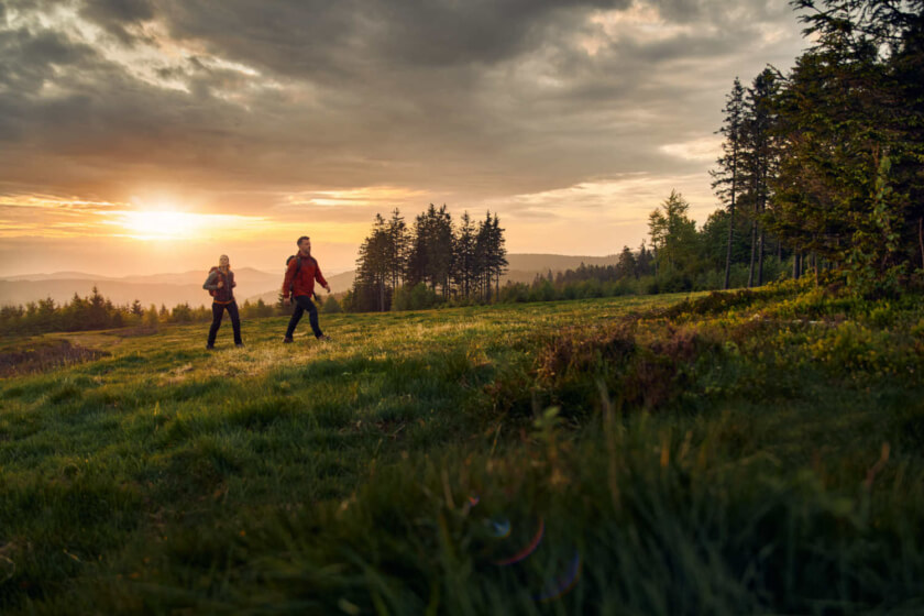 Ein Wanderpaar läuft bei Sonnenaufgang über eine saftig grüne Wiese