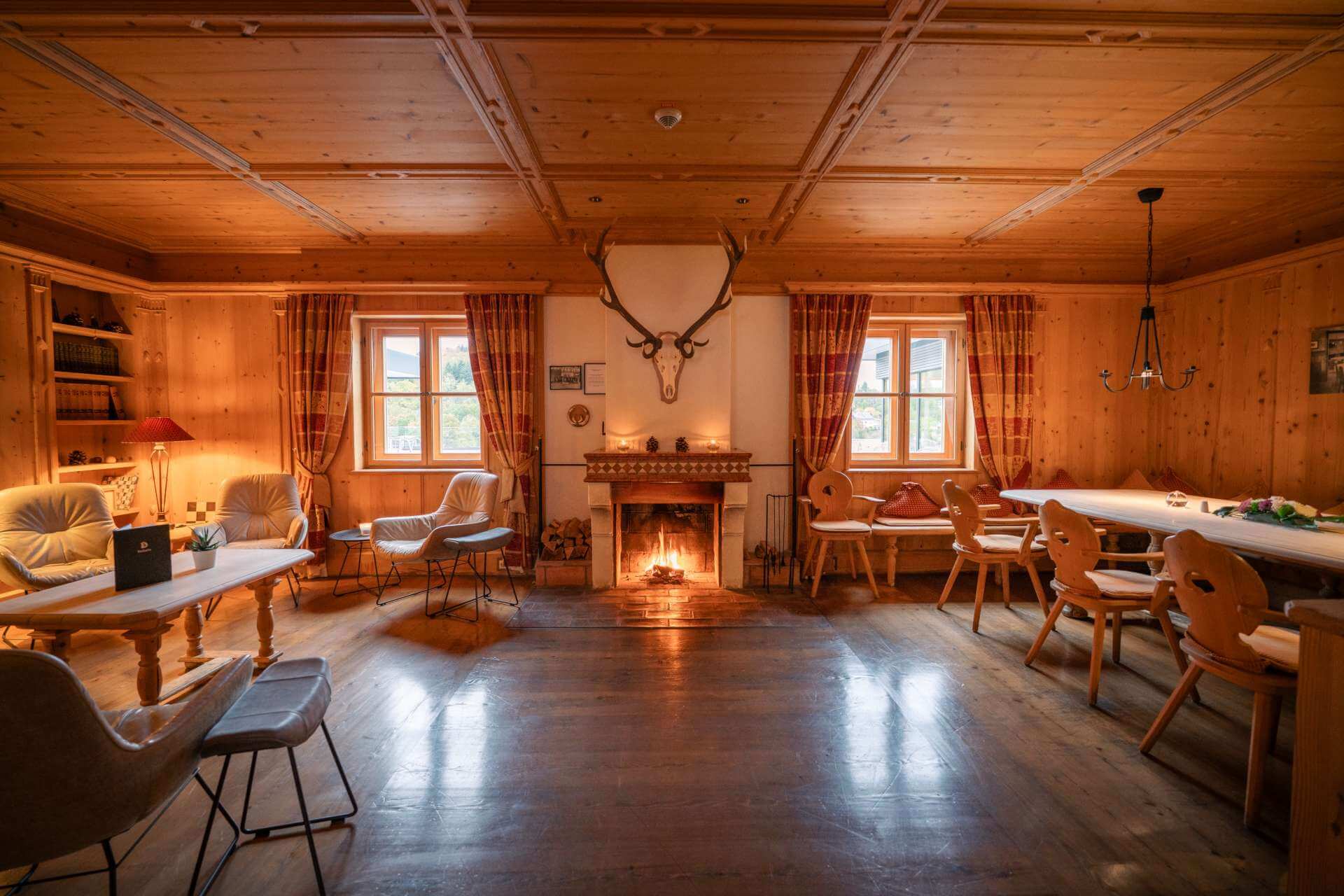 Holzgetäfelte Kaminstube mit Sesseln, Kamin und Hirschgeweih an der Wand