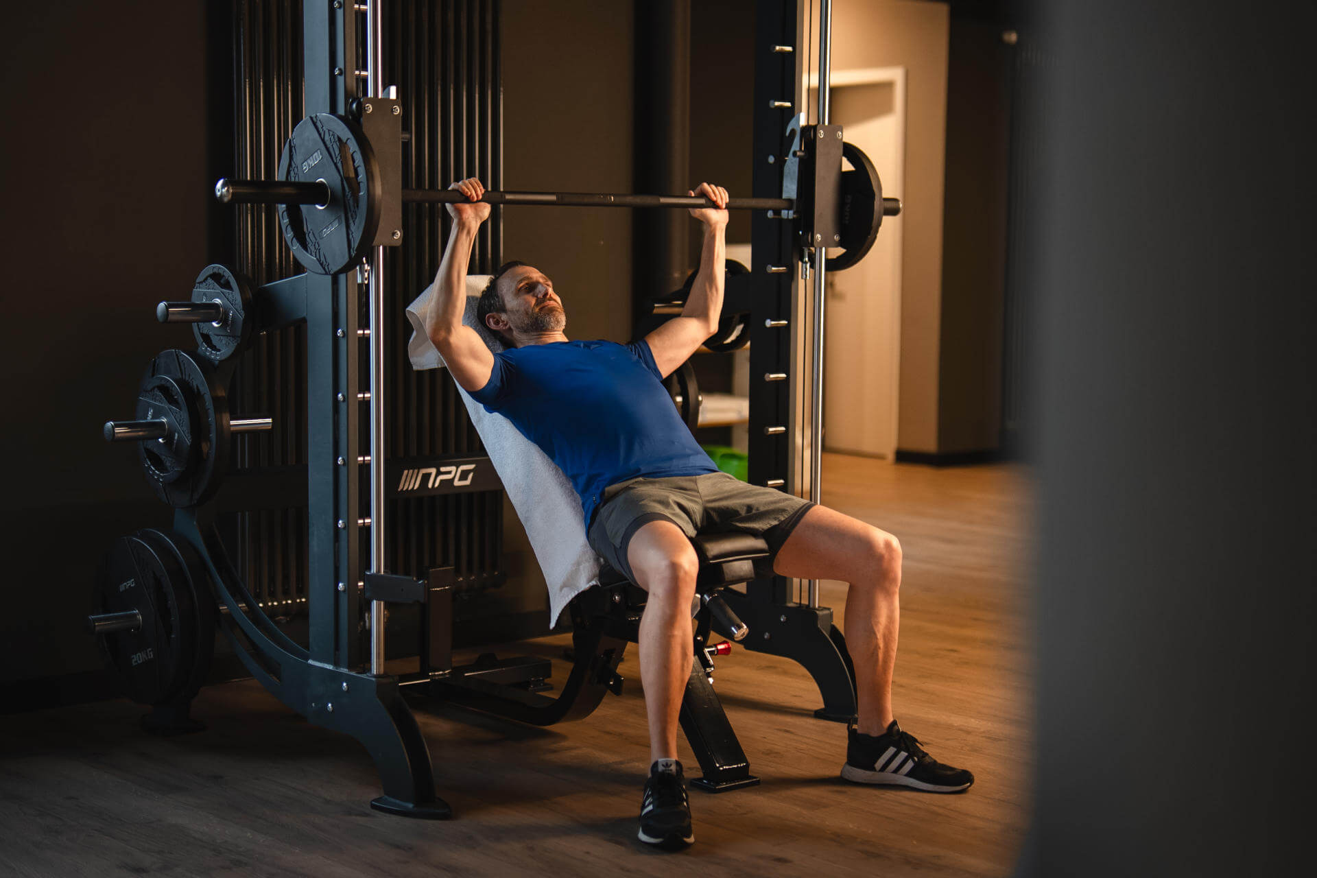 A man is working out on a multi-gym with a barbell in the gym.